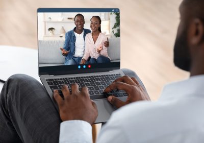 Marriage Therapy Online. Black counselor speaking with happy couple via video call on laptop computer, over shoulder view, selective focus